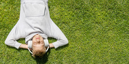 A boy relaxing on the grass, listening to music with headphones. flat lay