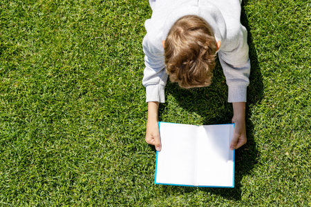 A boy reading a book on a grassy field. Flat lay with copy space