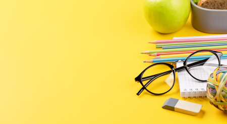 School supplies, stationery, and lunch box on yellow background. education and nutrition. With blank space for your textの写真素材