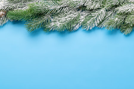 Christmas fir tree branch frame over blue background with space for greetings text. Flat lay
