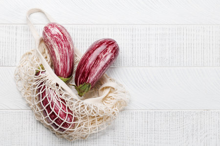 Eggplant, a glossy and fresh vegetable in mesh bag on wooden table. Flat lay with copy spaceの写真素材