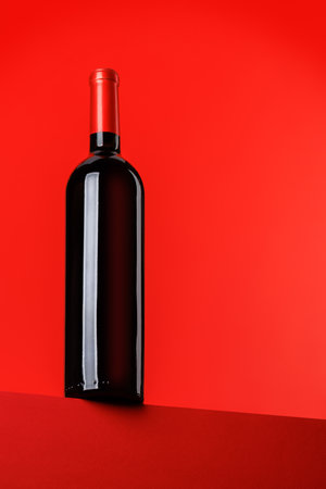 Red wine elegance: Wine bottle against vibrant red background. With copy spaceの写真素材