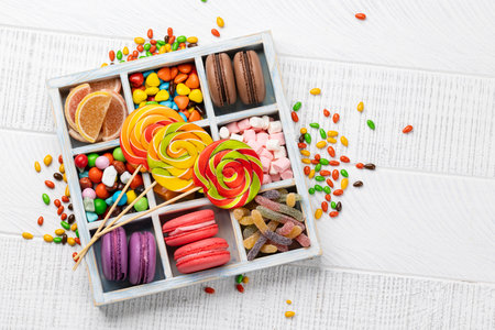 Various colorful candies, lollipops, and macaroons. Flat lay sweets in box over wooden background with copy spaceの写真素材