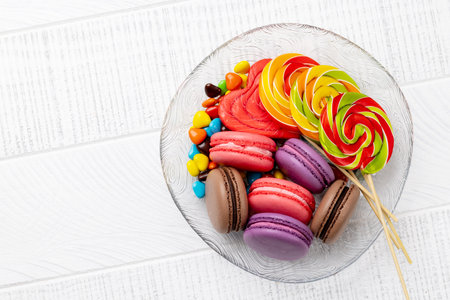 Various colorful candies, lollipops, and macaroons. Flat lay over wooden background with copy spaceの写真素材