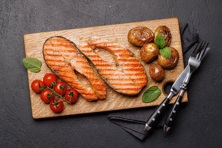 Grilled salmon steaks and potatoes on a wooden board, a mouthwatering delight. Flat layの写真素材
