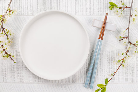 Empty plate on table adorned with cherry blossom branch and chopsticks, epitomizing Japanese food culture, providing ample copy spaceの写真素材