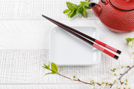 Empty plate on table adorned with cherry blossom branch and chopsticks, epitomizing Japanese food culture, providing ample copy spaceの写真素材