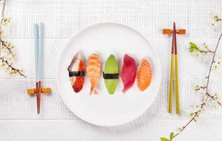 Sushi plate on table adorned with cherry blossom branch and chopsticks, epitomizing Japanese food cultureの写真素材