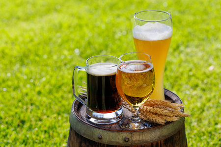 Variety of beer glasses on rustic wooden barrel. Sunny outdoor with copy spaceの写真素材