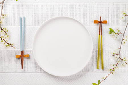 Empty plate on table adorned with cherry blossom branch and chopsticks, epitomizing Japanese food culture, providing ample copy spaceの写真素材