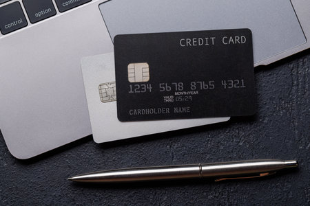 Black credit card on office table with laptop and supplies. Flat lay. Premium banking conceptの写真素材