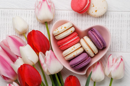 Pastel colorful tulips and vibrant macaroons fill a heart-shaped bowl, offering a delightful and charming scene perfect for celebrations or joyful momentsの写真素材