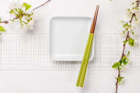 Empty plate on table adorned with cherry blossom branch and chopsticks, epitomizing Japanese food culture, providing ample copy spaceの写真素材