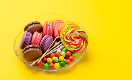 Various colorful candies, lollipops, and macaroons. Over yellow background with copy spaceの写真素材