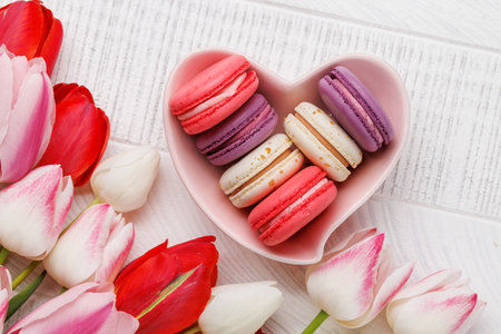 Pastel colorful tulips and vibrant macaroons fill a heart-shaped bowl, offering a delightful and charming scene perfect for celebrations or joyful momentsの写真素材