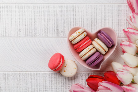 Pastel colorful tulips and vibrant macaroons fill a heart-shaped bowl, offering a delightful and charming scene perfect for celebrations or joyful momentsの写真素材
