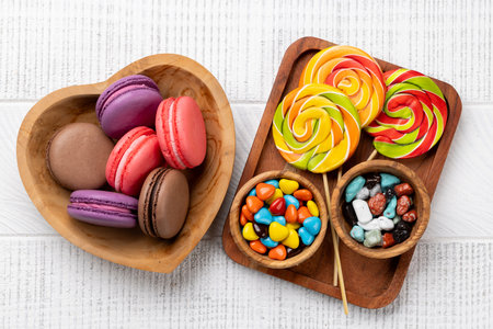 Various colorful candies, lollipops, and macaroons. Flat lay over wooden backgroundの写真素材