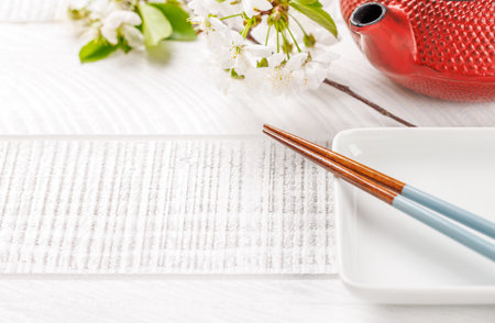 Empty plate on table adorned with cherry blossom branch and chopsticks, epitomizing Japanese food culture, providing ample copy spaceの写真素材