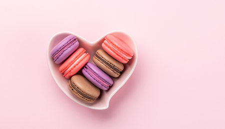 Various colorful macaroons in heart shaped bowl. Love sweets over pink background with copy spaceの写真素材