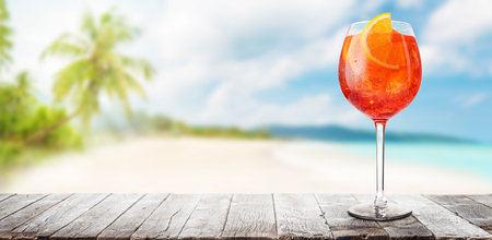 Glass of Spritz on a table with a stunning sea and beach background, perfect for a summer dayの写真素材