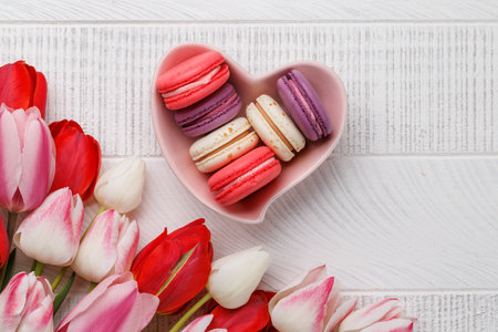 Pastel colorful tulips and vibrant macaroons fill a heart-shaped bowl, offering a delightful and charming scene perfect for celebrations or joyful momentsの写真素材