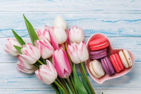 Pastel colorful tulips and vibrant macaroons fill a heart-shaped bowl, offering a delightful and charming scene perfect for celebrations or joyful momentsの写真素材