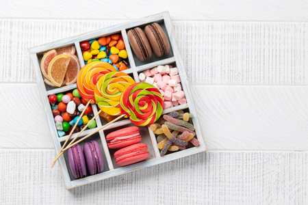 Various colorful candies, lollipops, and macaroons. Flat lay sweets in box over wooden background with copy spaceの写真素材