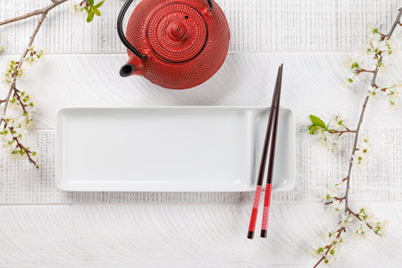 Empty plate on table adorned with cherry blossom branch and chopsticks, epitomizing Japanese food culture, providing ample copy spaceの写真素材
