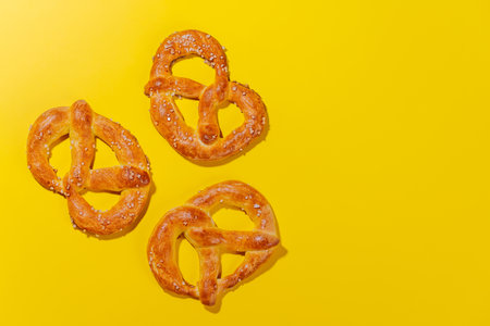 Pretzels scattered across a bright yellow background. The pretzels are golden-brown, perfectly baked, and sprinkled with coarse saltの写真素材