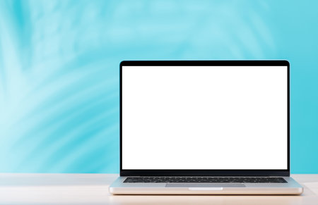 Laptop with a blank white screen placed on a table, wall in the background casting warm light and...