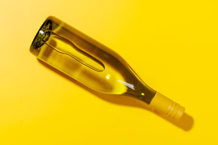 A white wine bottle placed flat on a yellow background in a flat lay style, creating a vibrant and...