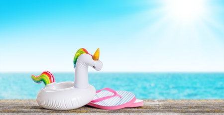 flip flops and a floating unicorn placed on a table with a sunny sea background, embodying a fun, relaxed summer vibeの写真素材