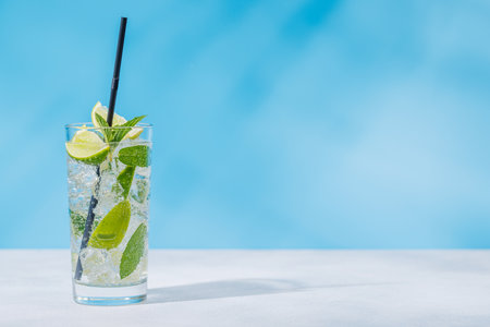 A mojito cocktail arranged on a table against a light blue background, enhanced by sunny glares and...