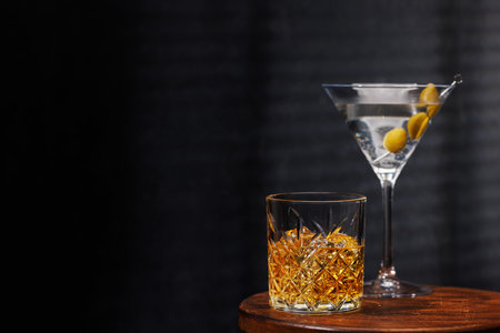 A whiskey glass and martini cocktail resting on a wooden table, set against a dark background, evoking a warm, rustic atmosphereの写真素材