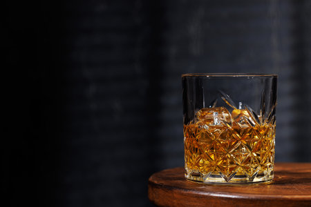 A whiskey glass resting on a wooden table, set against a dark background, evoking a warm, rustic atmosphereの写真素材