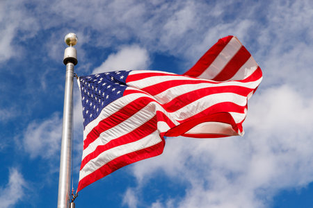 American flag waving against a sunny blue sky, showcasing patriotic pride with vivid colorsの写真素材