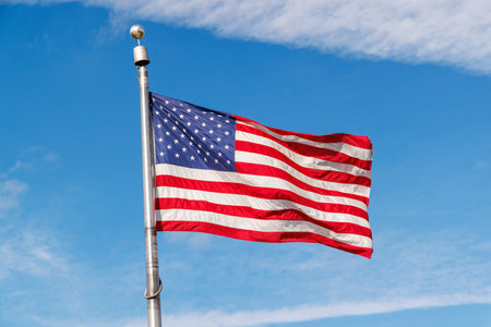 American flag waving against a sunny blue sky, showcasing patriotic pride with vivid colorsの写真素材