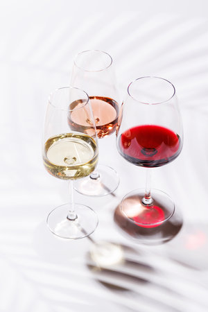 Three wine glasses filled with red, white, and rose wine, standing gracefully on a bright, minimalist background. A vibrant display of wine's variety and eleganceの写真素材