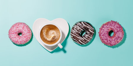An assortment of vibrant donuts with colorful toppings and a coffee cup on a heart-shaped saucer, arranged on a blue background in a flat lay style, perfect for a Valentines Day cardの写真素材