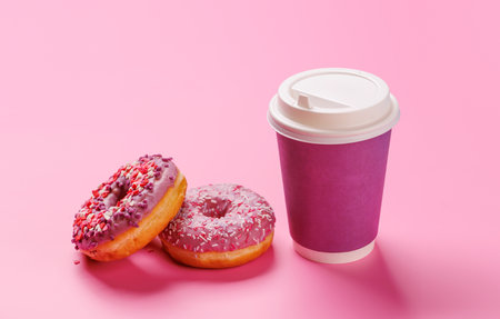 A cheerful display of donuts and a paper coffee cup on a pastel pink background. A sweet and vibrant setup for dessert or coffee themesの写真素材