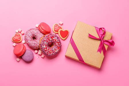 An eye-catching arrangement of colorful macarons and donuts and gift box on a pastel pink background. Perfect for showcasing desserts or sweet treats with a playful and vibrant aestheticの写真素材
