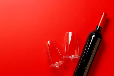 Elegant red wine glasses and a matching red wine bottle set against a deep red background, creating a luxurious and sophisticated sceneの写真素材