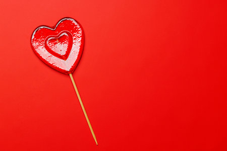 Heart-shaped lollipop on a vibrant red background with ample copy space, perfect for Valentine's Day themes, symbolizing sweetness and loveの写真素材