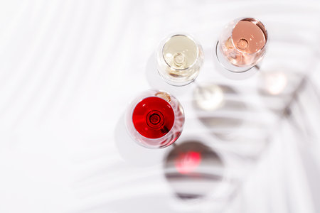 Three wine glasses filled with red, white, and rose wine, standing gracefully on a bright, minimalist background. A vibrant display of wine's variety and eleganceの写真素材