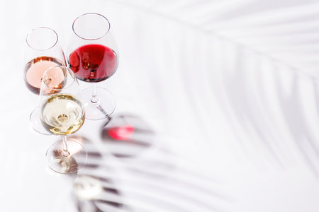 Three wine glasses filled with red, white, and rose wine, standing gracefully on a bright, minimalist background. A vibrant display of wine's variety and eleganceの写真素材