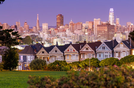 Vibrant sunset view of the Painted Ladies in San Francisco, iconic Victorian houses glowing under the warm hues of a colorful sky, with the city skyline in the backgroundの写真素材