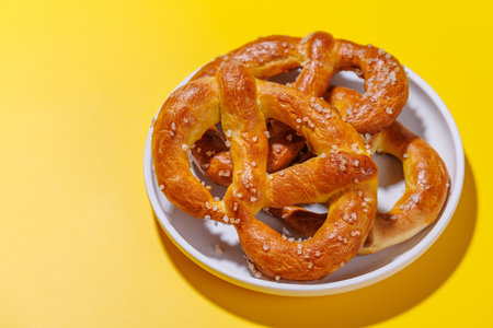 Pretzels scattered across a bright yellow background. The pretzels are golden-brown, perfectly baked, and sprinkled with coarse saltの写真素材