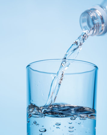 Crystal clear water being poured into a transparent glass with ice, creating refreshing ripples and...