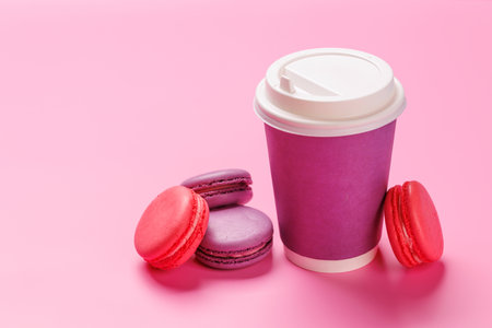 A vibrant arrangement of colorful macarons paired with a paper coffee cup on a pastel pink background. Perfect for coffee break, dessert, or celebratory themesの写真素材