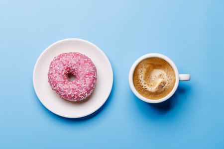 A vibrant donut with colorful toppings and a coffee cup arranged on a blue background in a flat lay style, creating a cheerful and appetizing sceneの写真素材